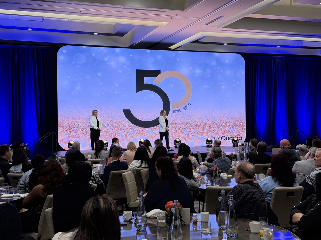 Presenters on stage in front of a wide 50th anniversary LED wall in Vancouver